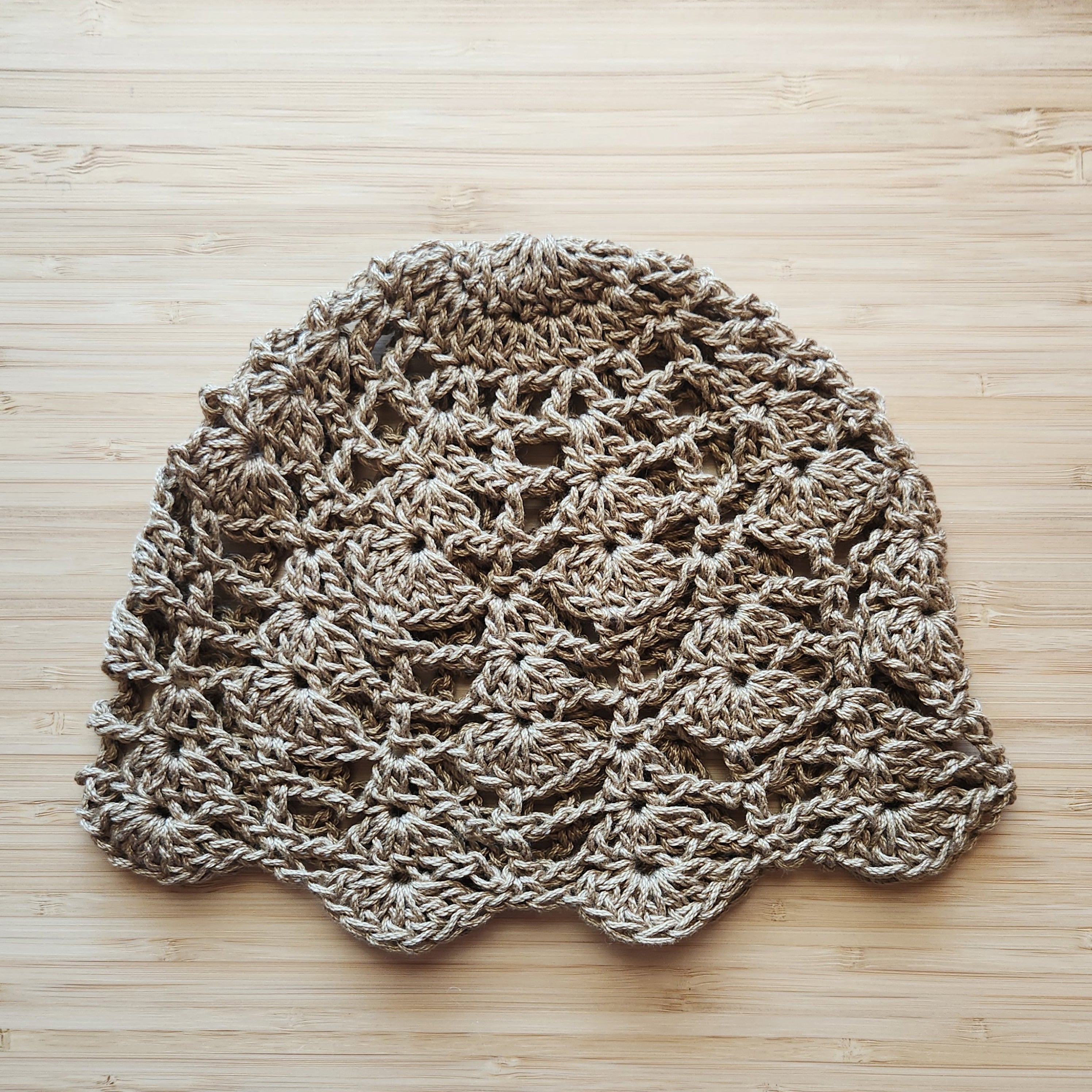 Taupe crocheted bohemian lace skull cap on a wooden surface.