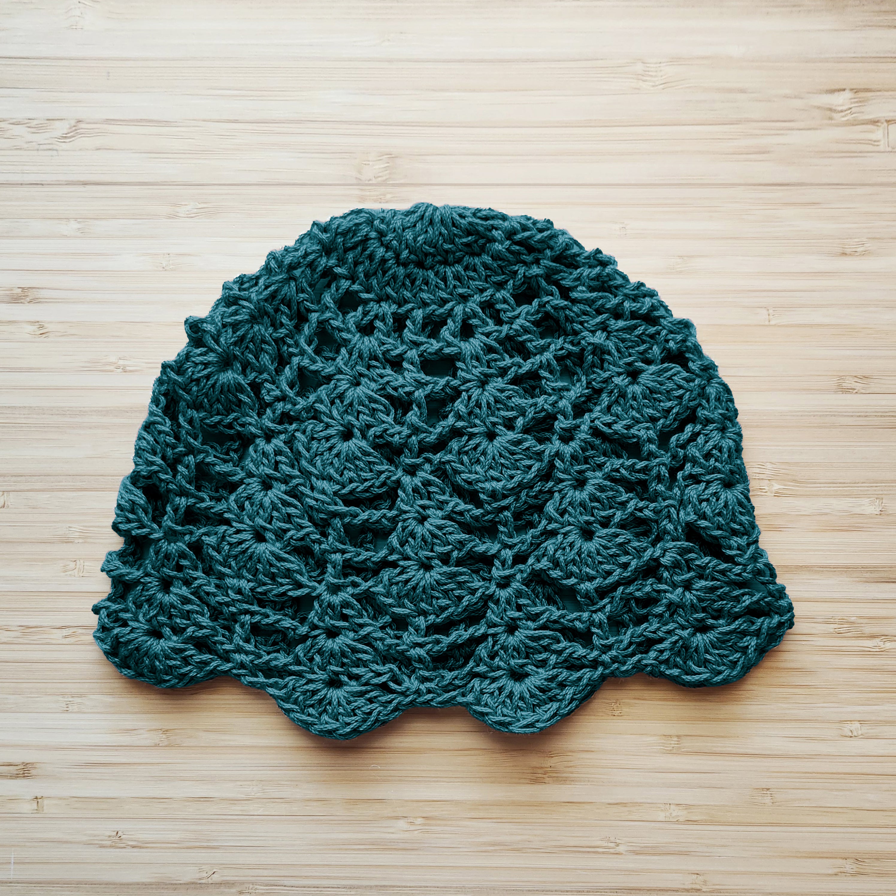 Teal crocheted hat with a floral pattern on a wooden surface.