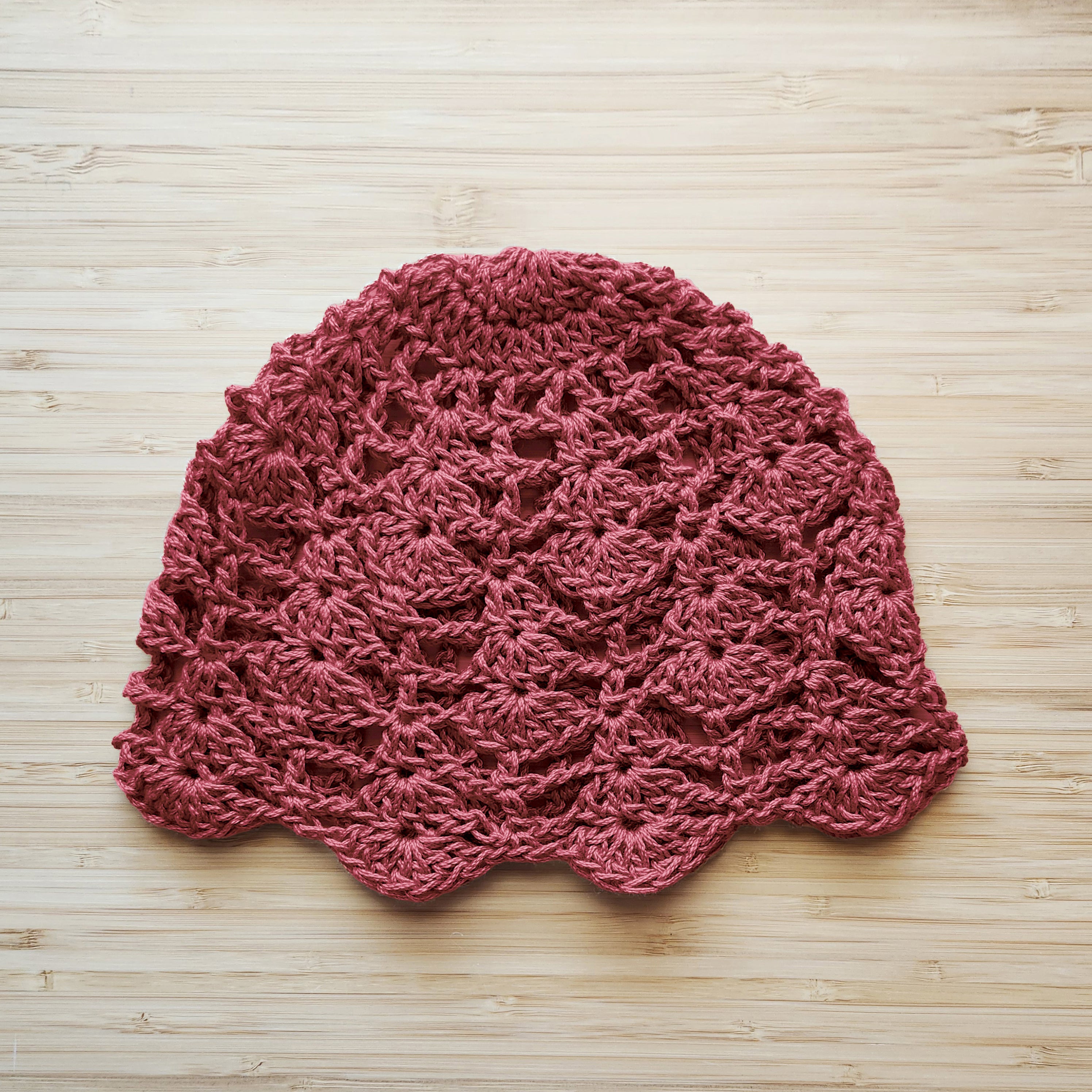 Terracotta pink crochet hat on a wooden surface.