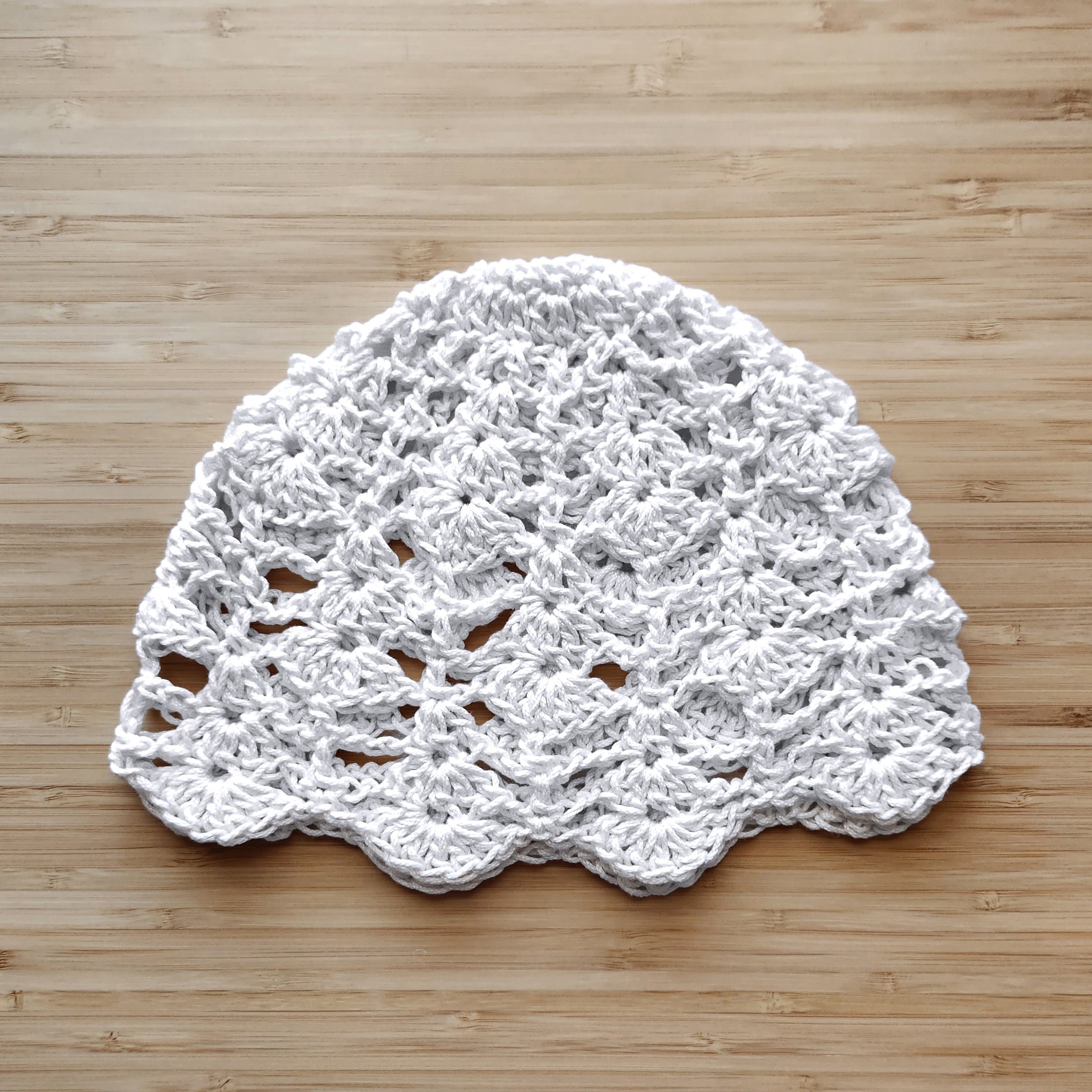 White crocheted boho lace summer cap on a wooden surface.