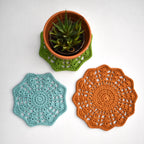 Three crocheted doilies in green, blue, and orange on a white background with a small potted plant.