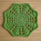 Green crocheted floral hexagon doily on a wooden surface.