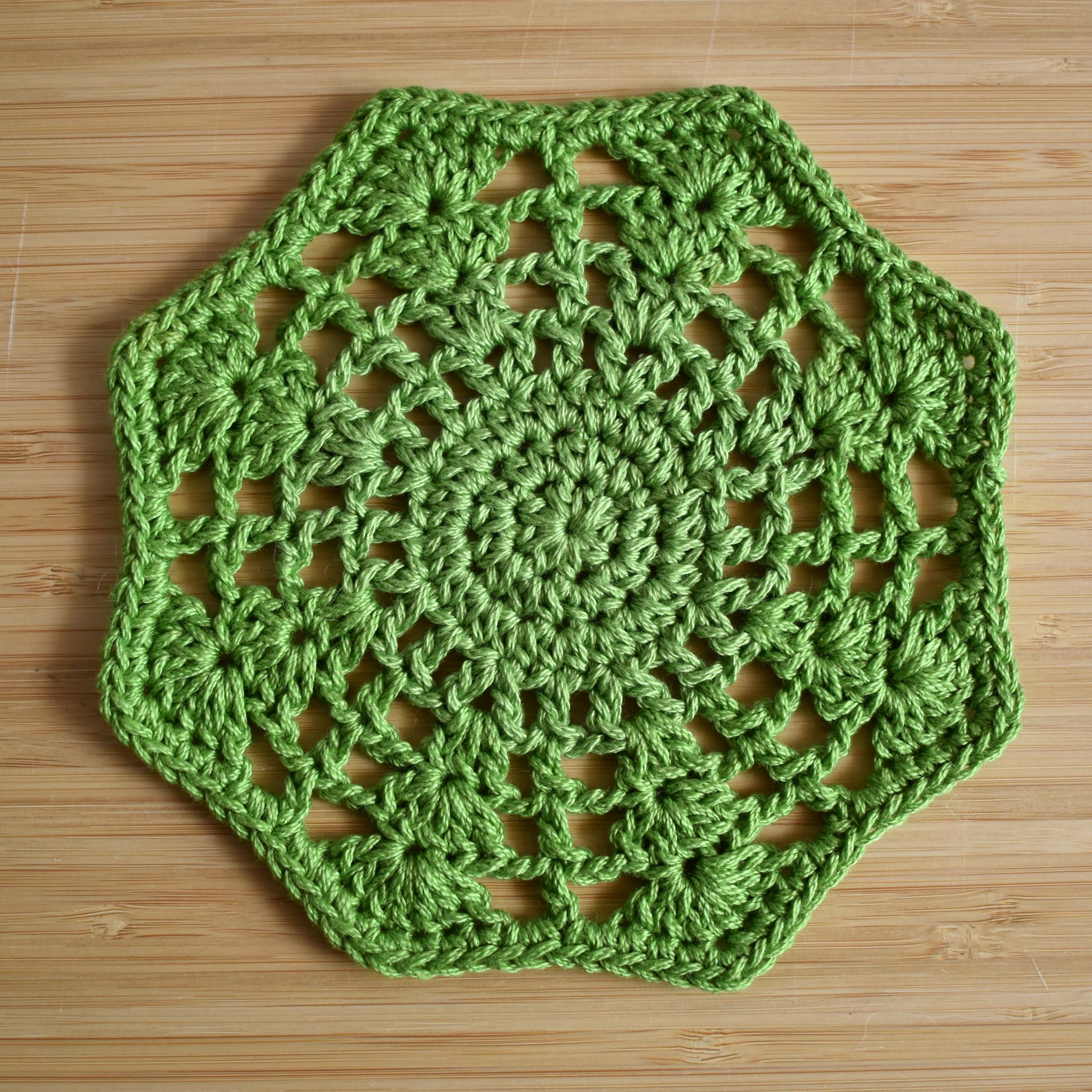 Green crocheted floral hexagon doily on a wooden surface.