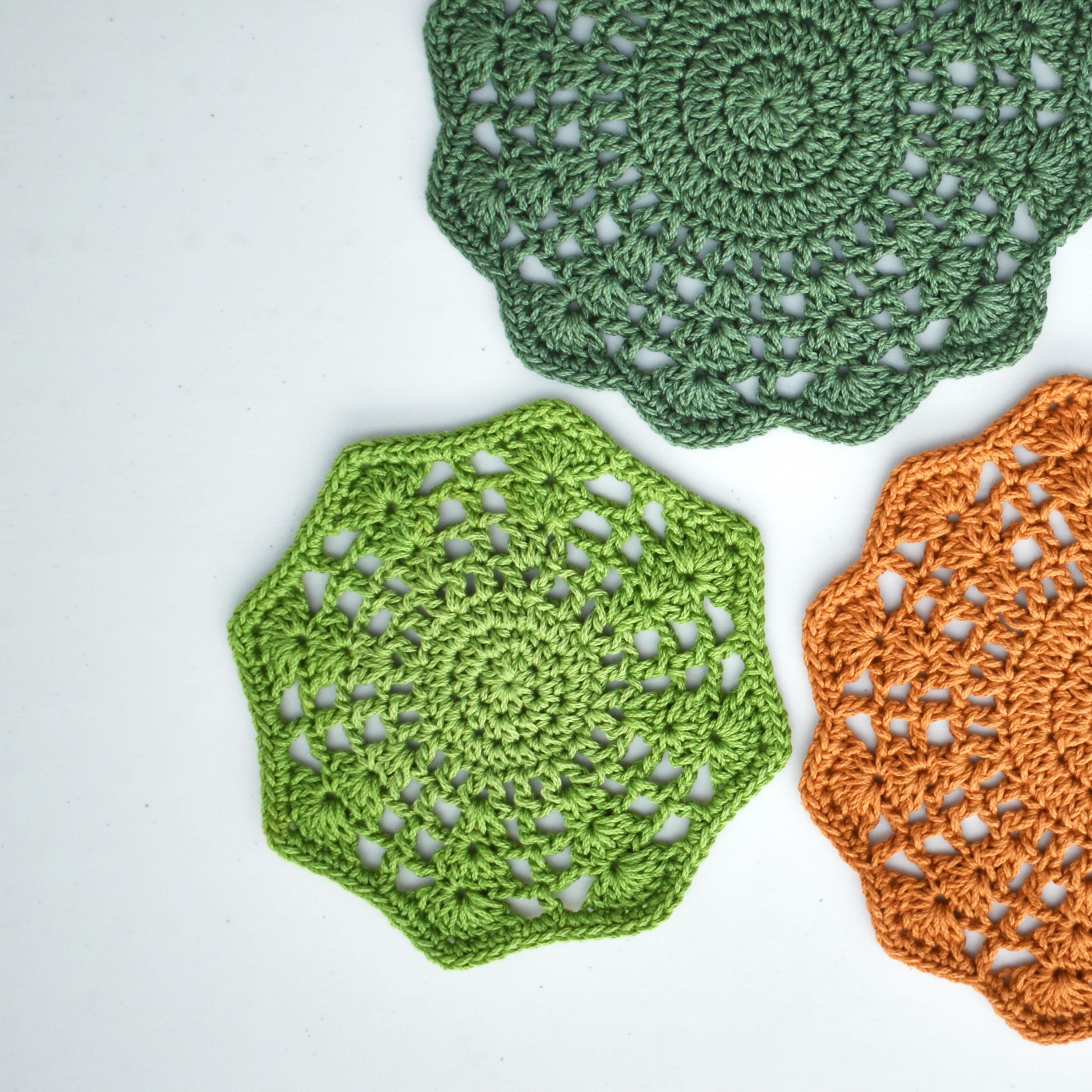 Three crocheted floral doilies in green and orange on a white background.