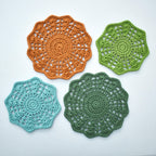 Four crocheted floral doilies in orange, green, and blue on a white background.