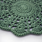 Close-up of a green crocheted doily with a textured floral pattern on a white background.