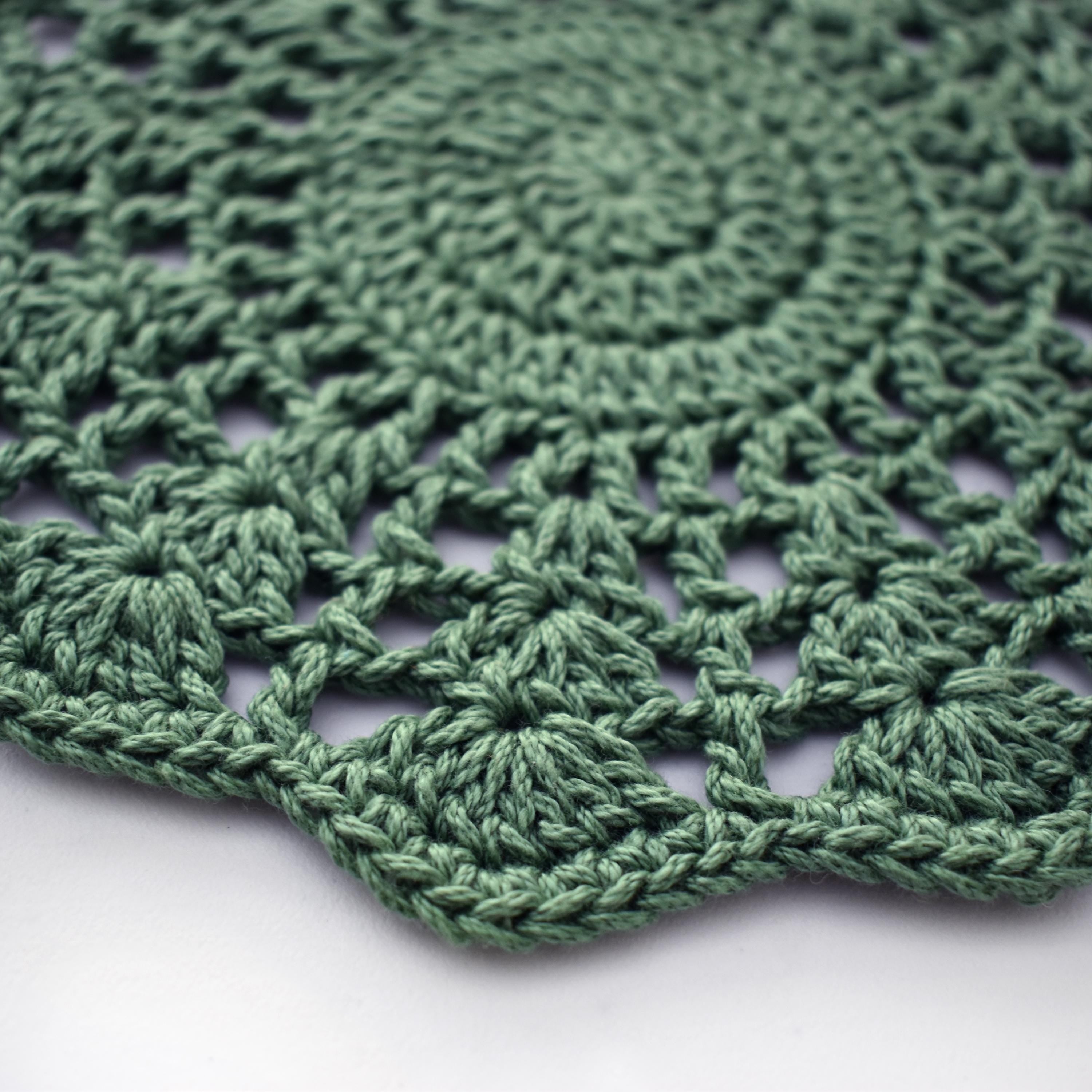 Close-up of a green crocheted doily with a textured floral pattern on a white background.