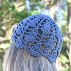 A woman wearing a blue lace skull cap looking into a blurred natural outdoor background.