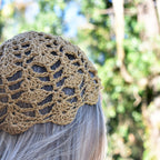 Khaki brown crochet hat worn by a person with blurred green foliage in the background.