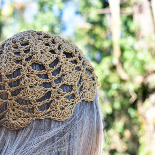 Khaki brown crochet hat worn by a person with blurred green foliage in the background.