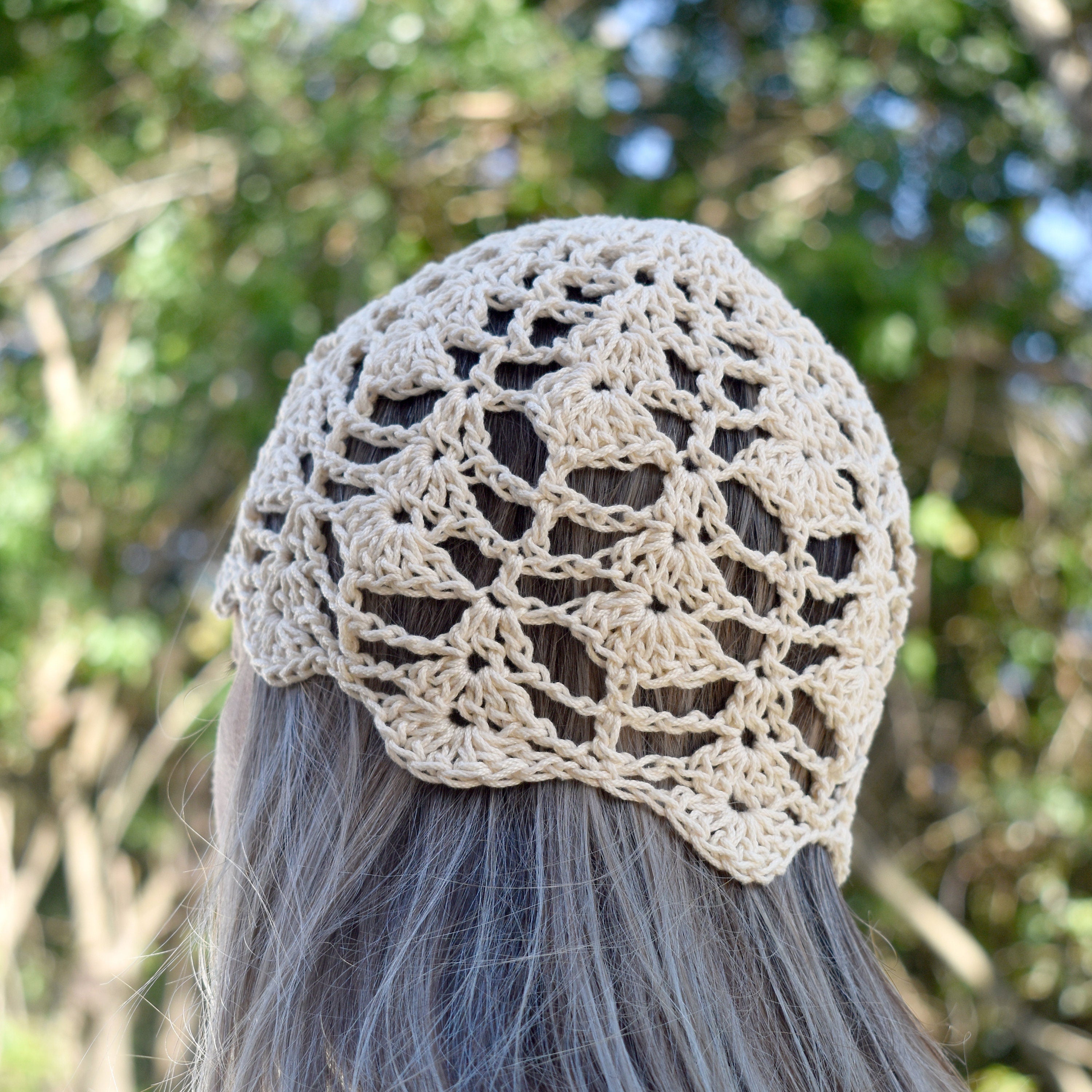 A person wearing a beige crochet skull cap against blurred green foliage in the background.