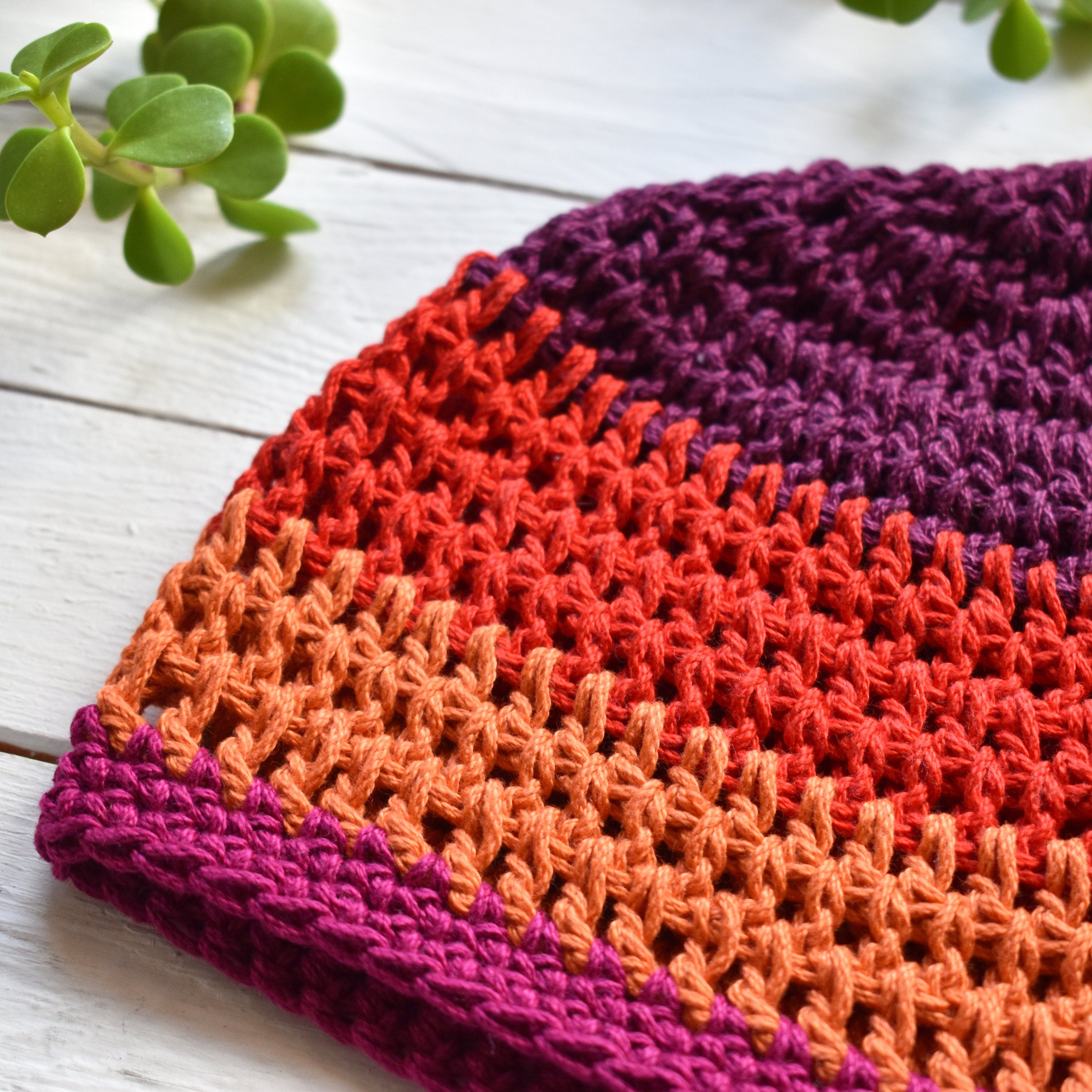 Crocheted beanie with a gradient of red, orange, and purple on a white wooden surface.