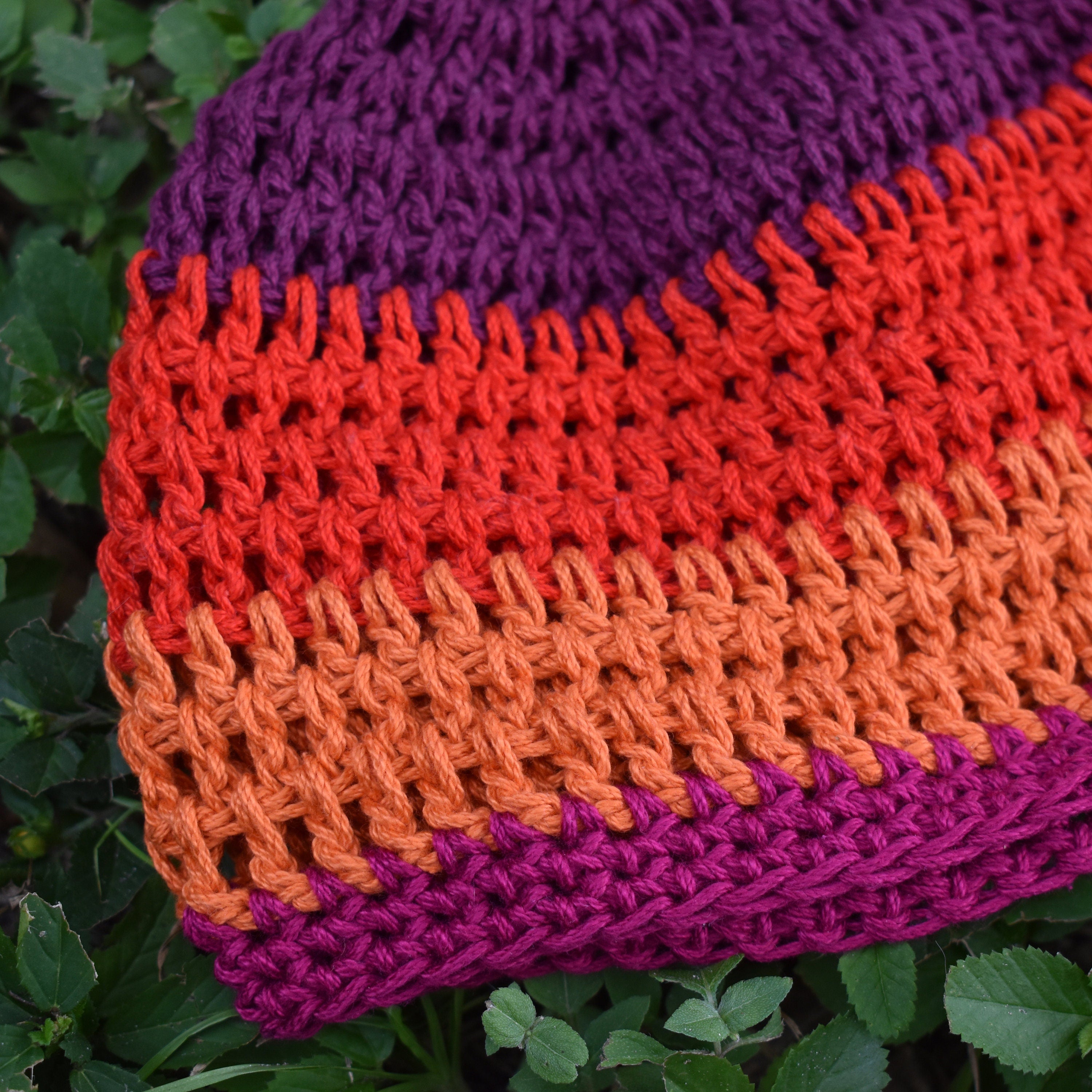 Close-up of a colorful knitted hat with purple, orange, and red stripes on a green leaf background.