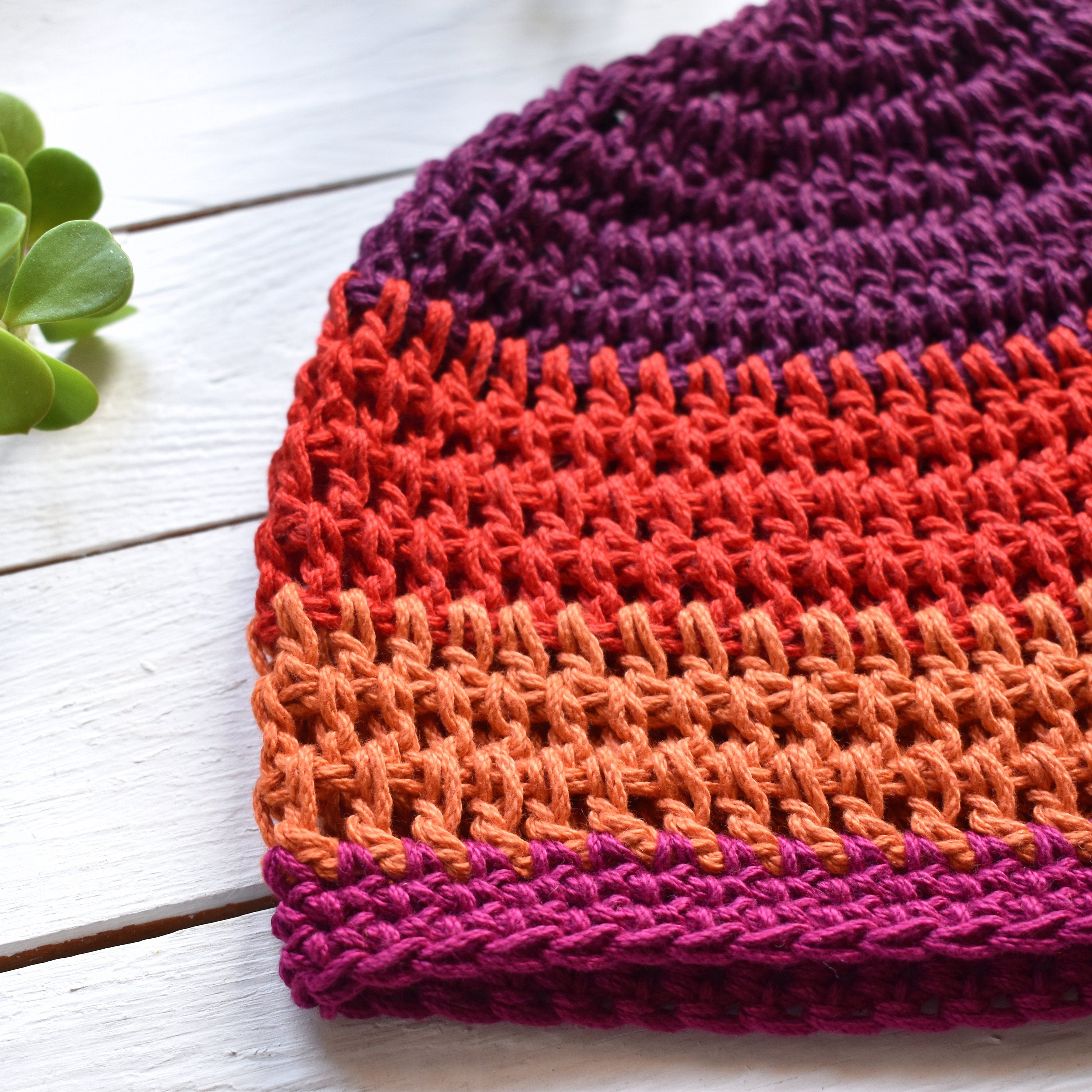 A close-up of a colorful crocheted hat on a white wooden surface with a green leaf.