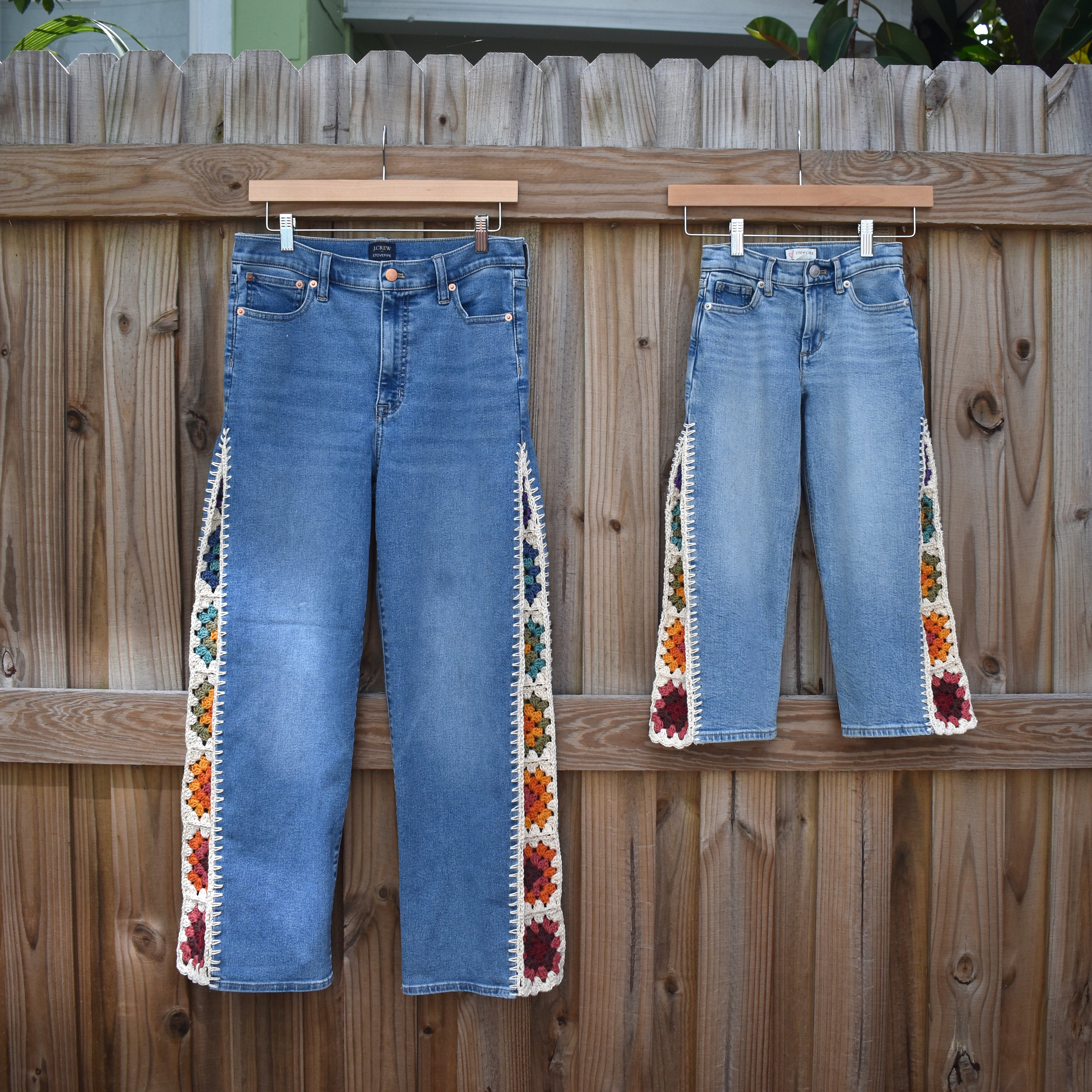 Two pairs of matching mother and daughter J. Crew blue jeans with crochet granny square inserts hanging on a wooden fence.
