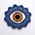 Blue crocheted flower with a brown eye in the center on a white background.