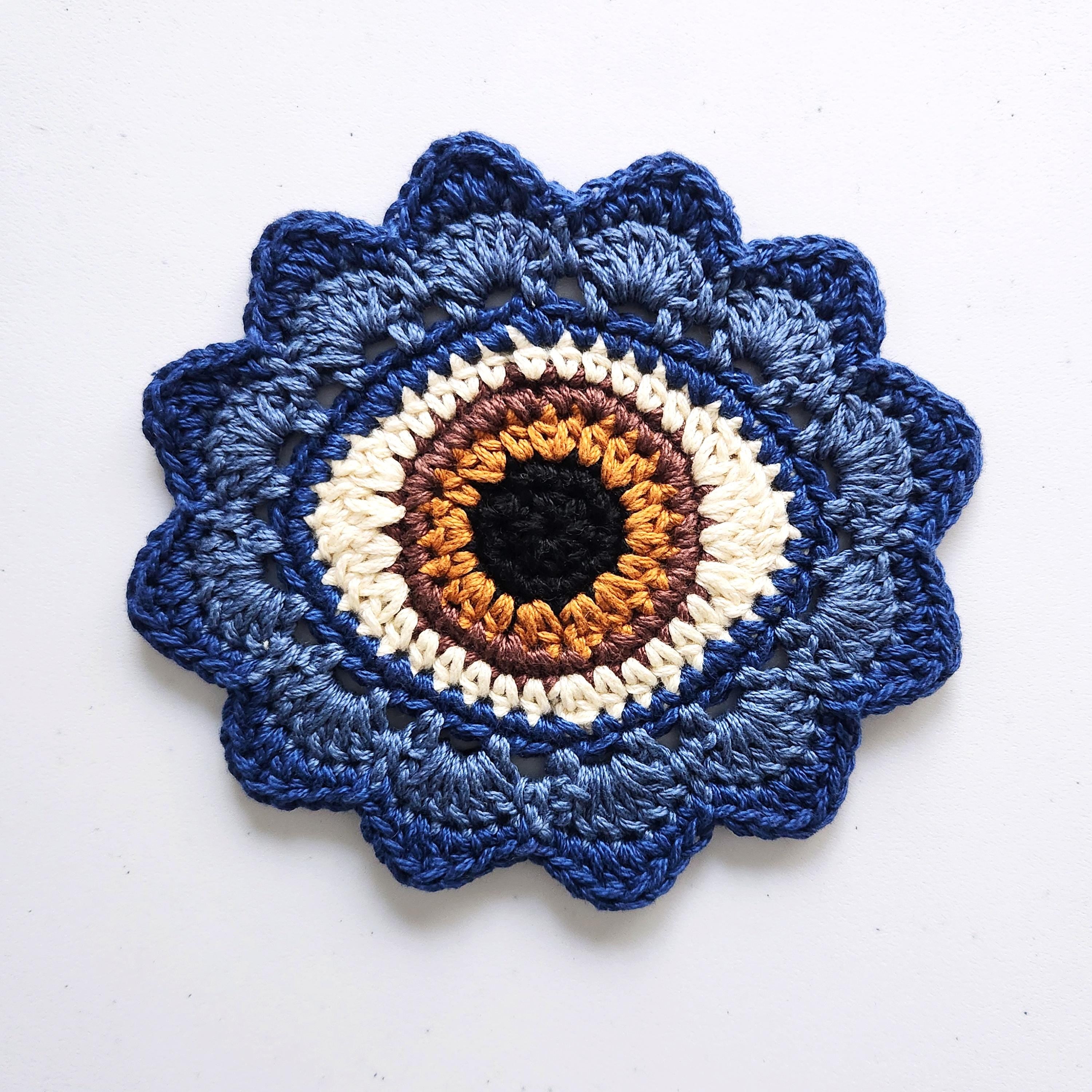 Blue crocheted flower with a brown eye in the center on a white background.
