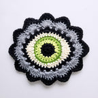 Crocheted flower pattern with a green eye in the center on a white background.
