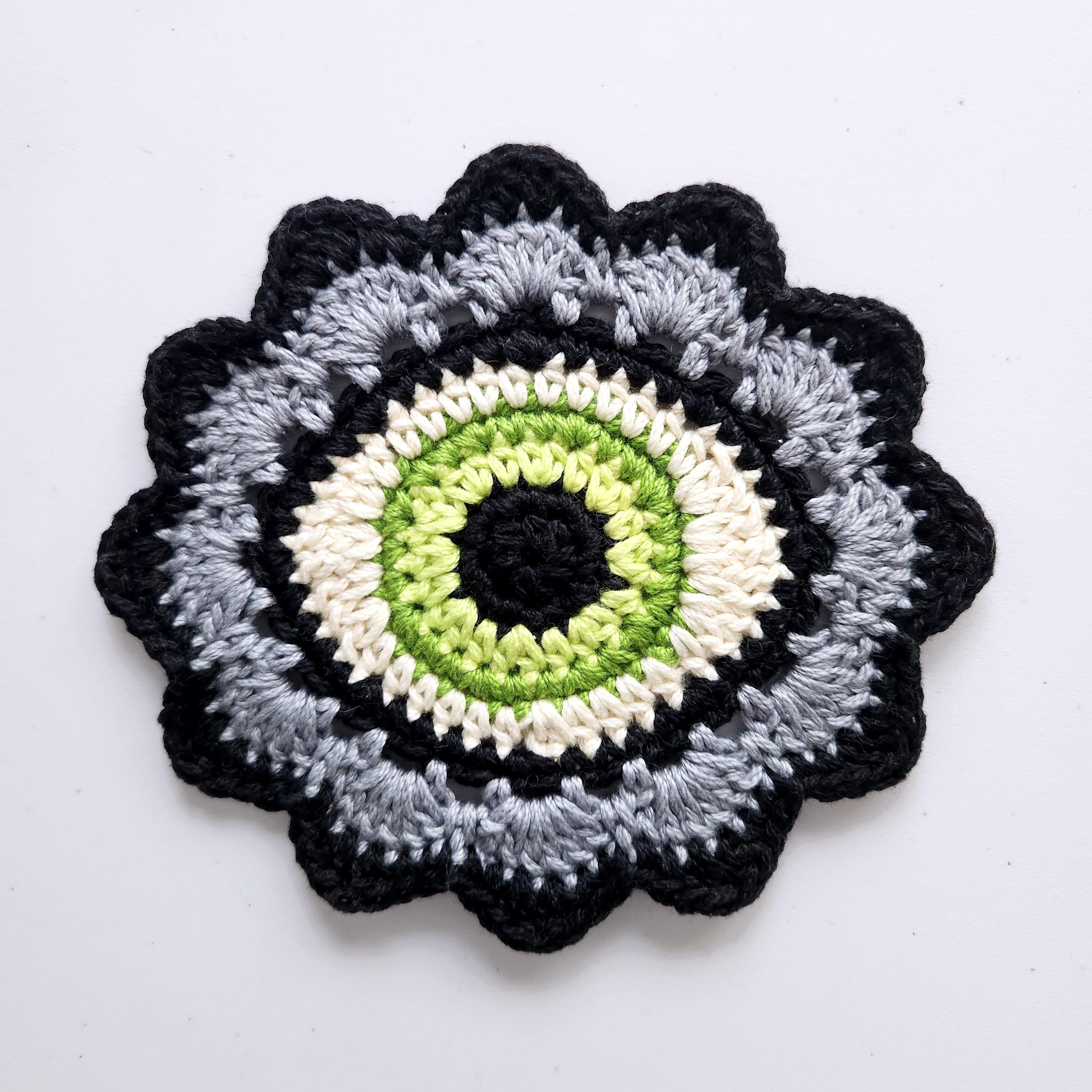 Crocheted flower pattern with a green eye in the center on a white background.