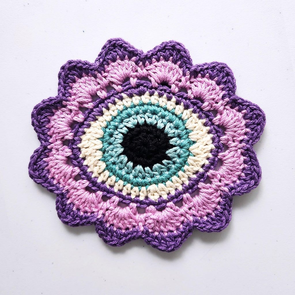 Crocheted flower with a sky blue eye in the center on a white background.