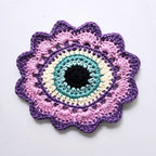 Crocheted flower with a sky blue eye in the center on a white background.