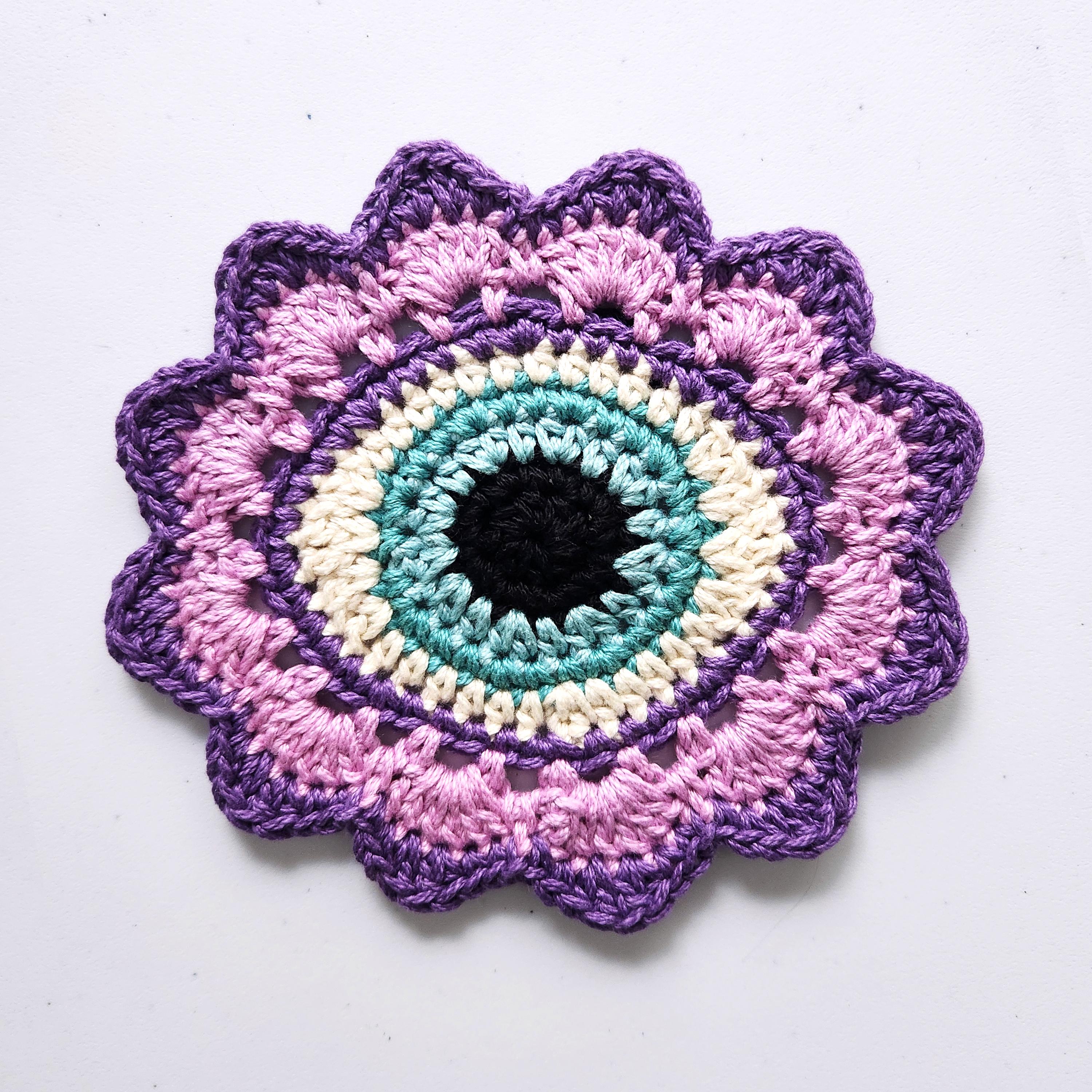 Crocheted flower with a sky blue eye in the center on a white background.