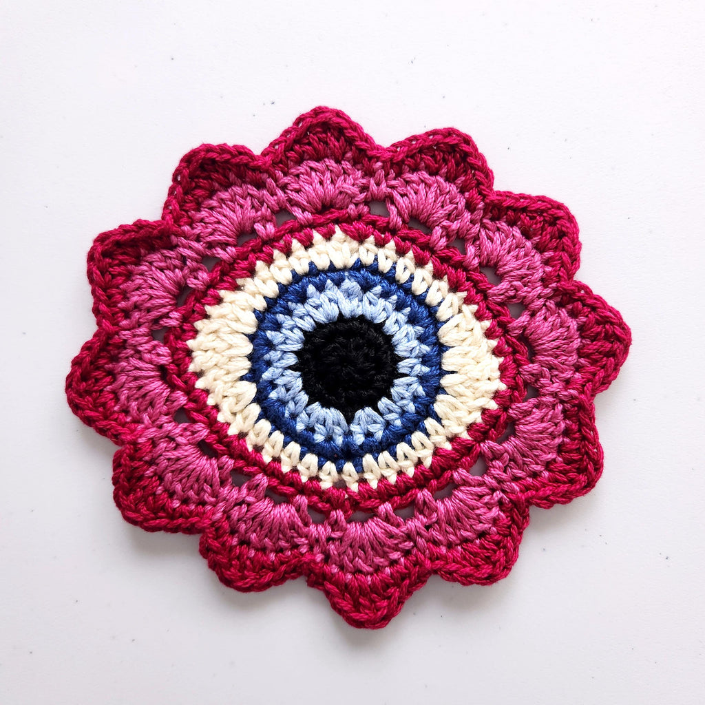 Crocheted flower with a blue eye in the center on a white background.