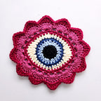 Crocheted flower with a blue eye in the center on a white background.