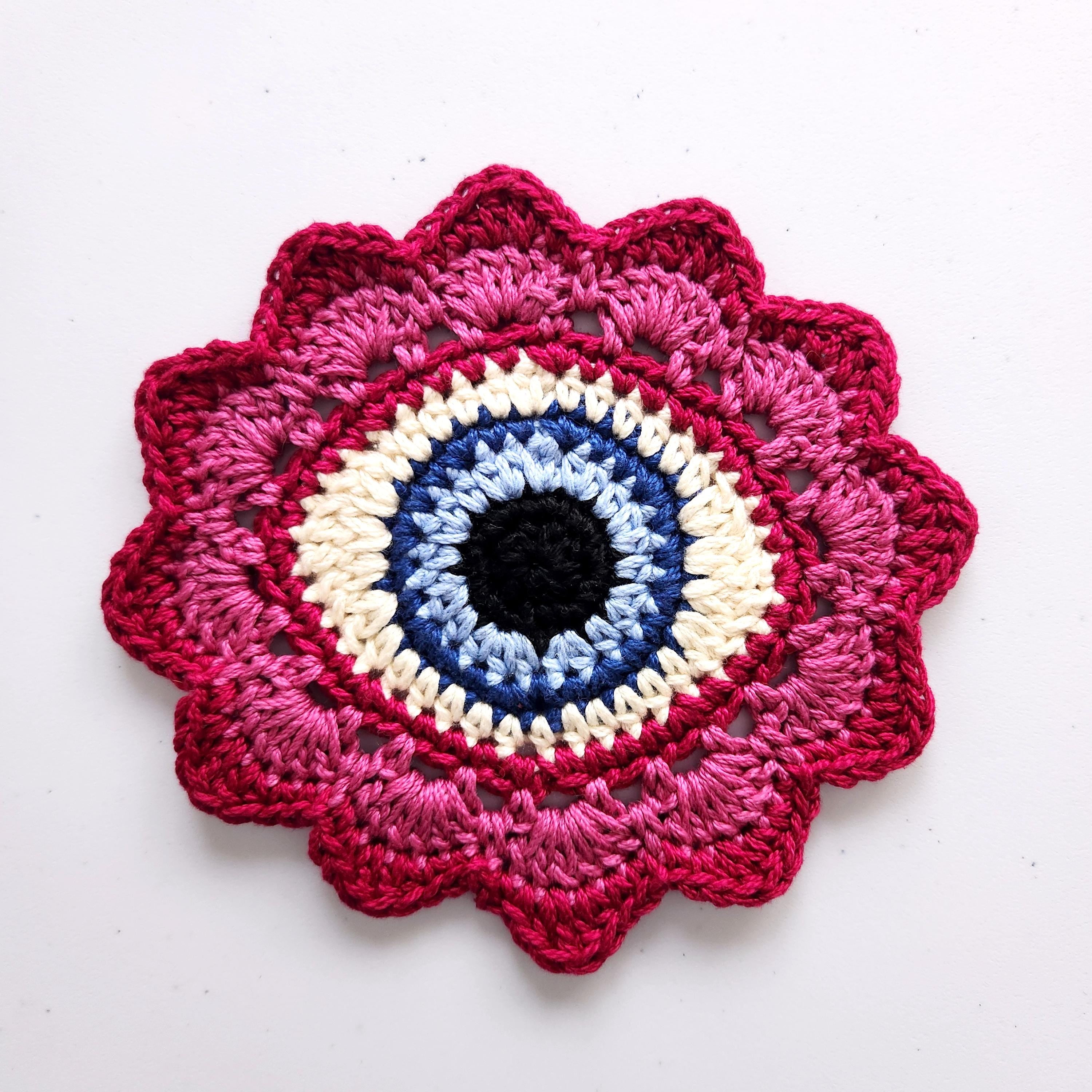 Crocheted flower with a blue eye in the center on a white background.