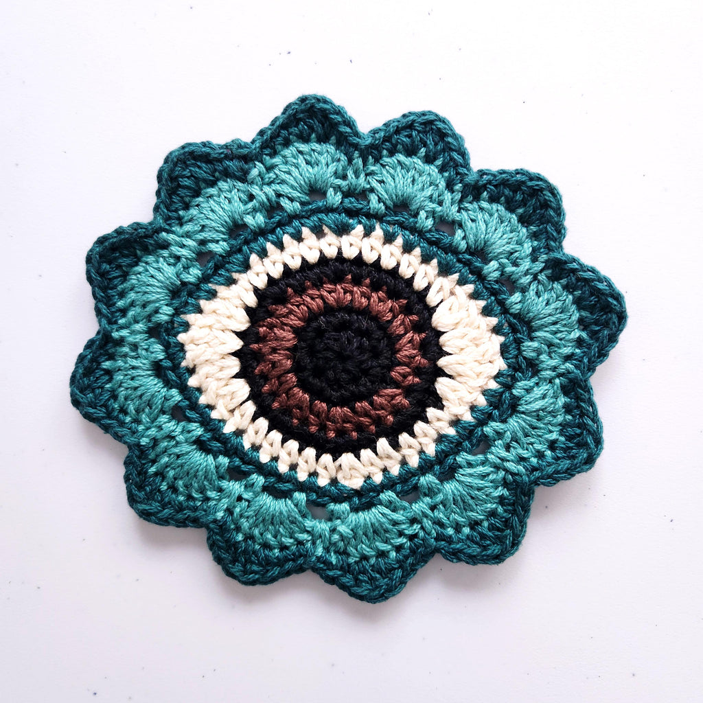 Crocheted flower with a brown eye in the center on a white background.