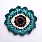 Crocheted flower with a brown eye in the center on a white background.