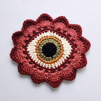 Crocheted flower with hazel eye in the center on a white background.