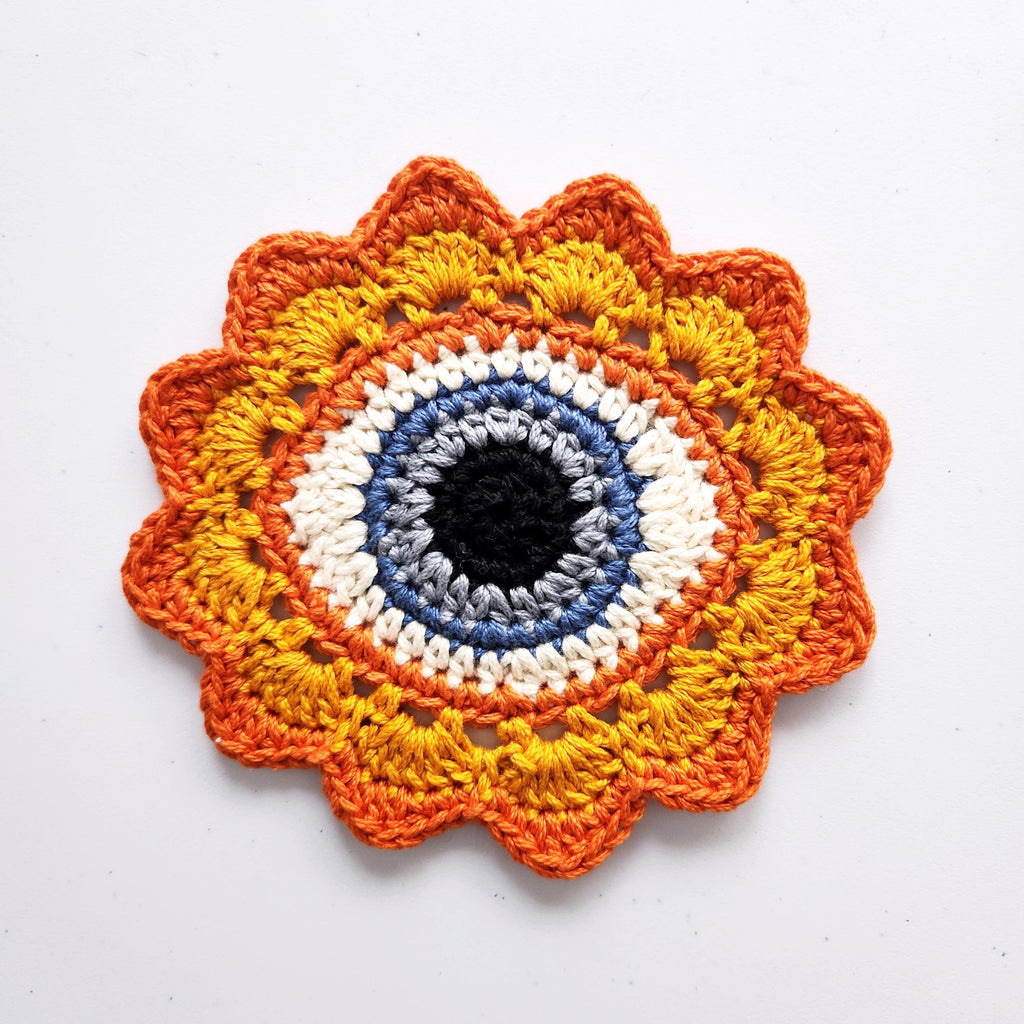 Crocheted flower pattern with a gray-blue eye in the center on a white background.