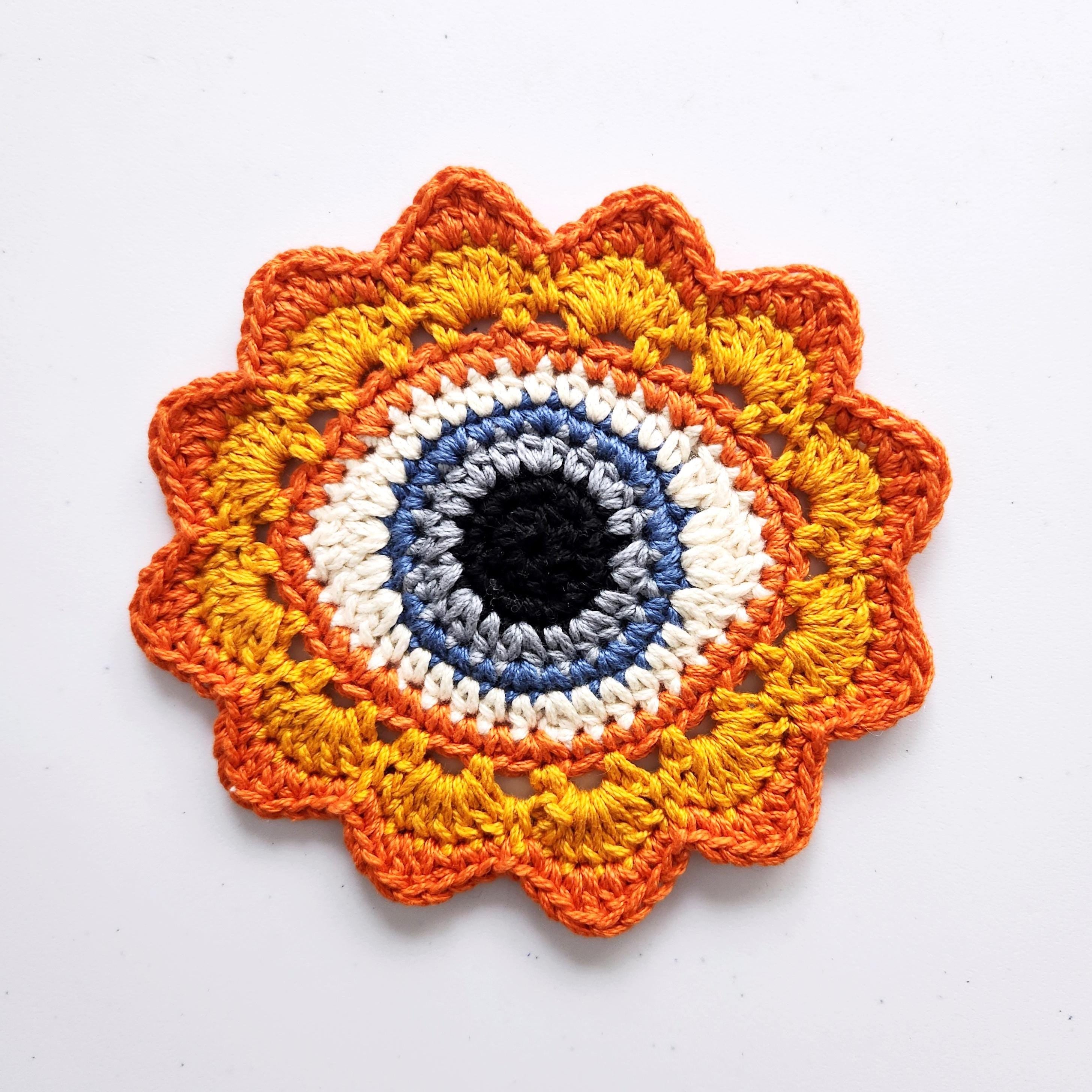 Crocheted flower pattern with a gray-blue eye in the center on a white background.