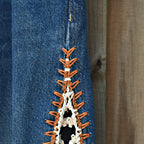 Close-up of a blue denim garment with a decorative orange and white crochet or knotted trim detail along a seam, set against a wooden background.