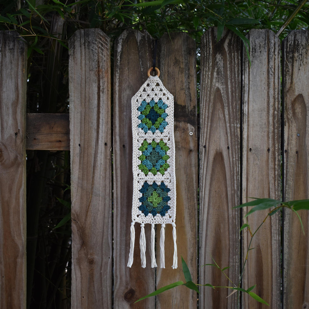 Crocheted wall hanging with geometric pattern on a old wooden fence.