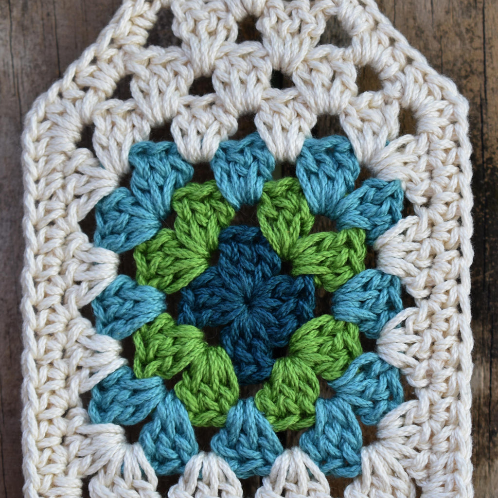 Crocheted square with a blue and green granny square on a wooden background.