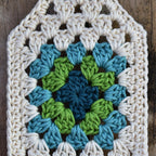 Crocheted square with a blue and green granny square on a wooden background.