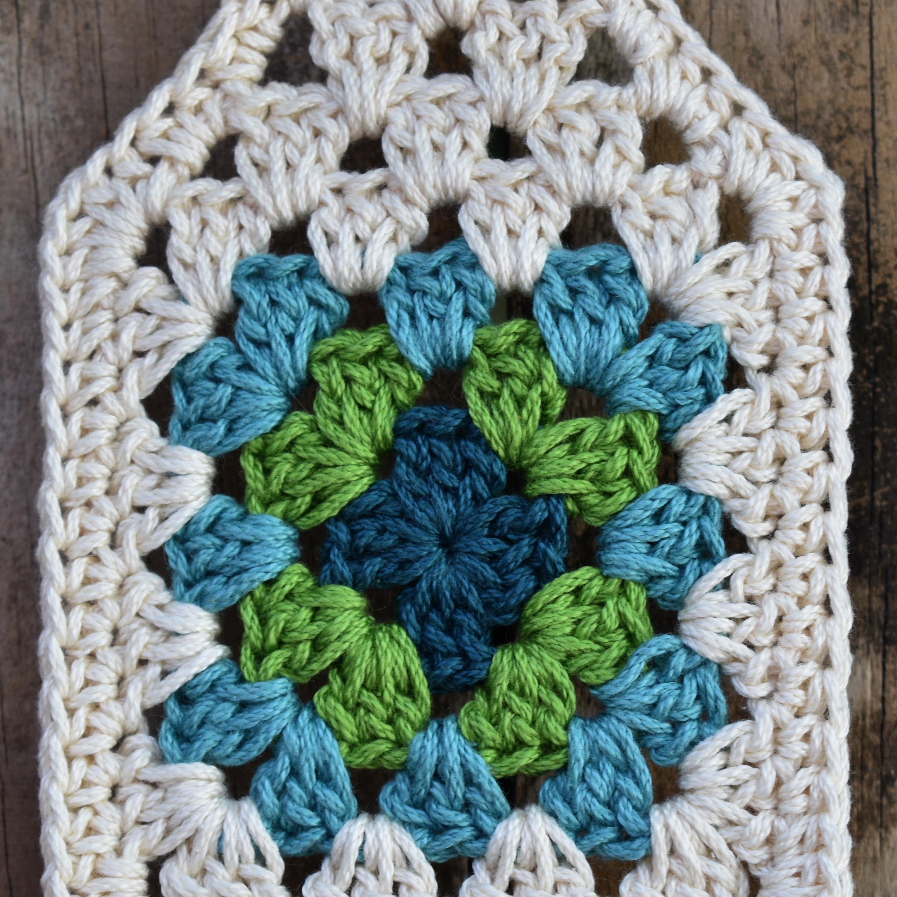 Crocheted square with a blue and green granny square on a wooden background.