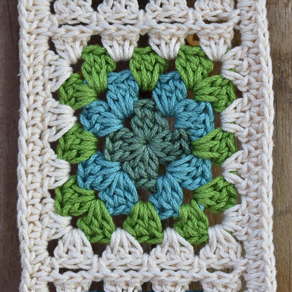 Crocheted square with a green and blue granny square on a wooden surface.