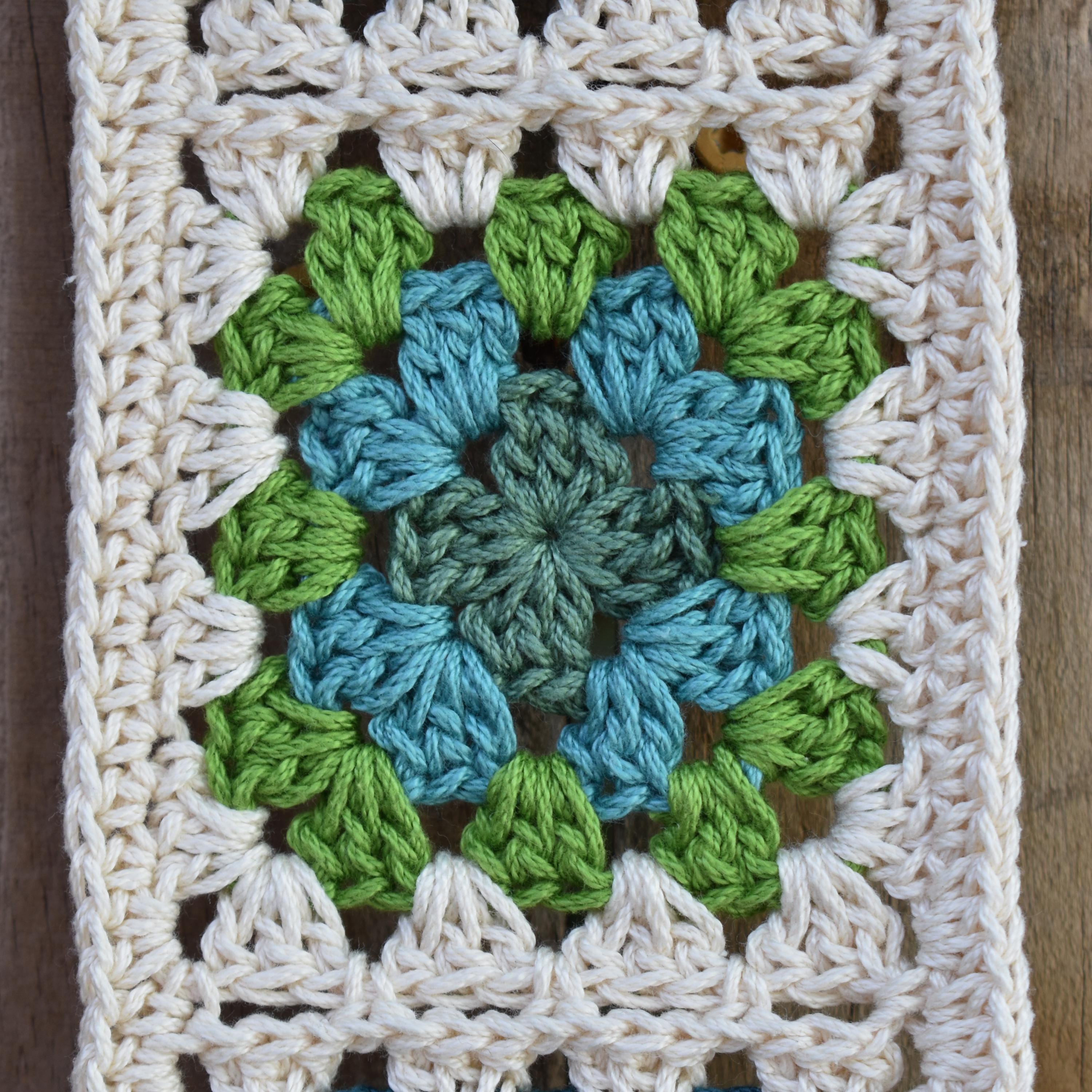 Crocheted square with a green and blue granny square on a wooden surface.
