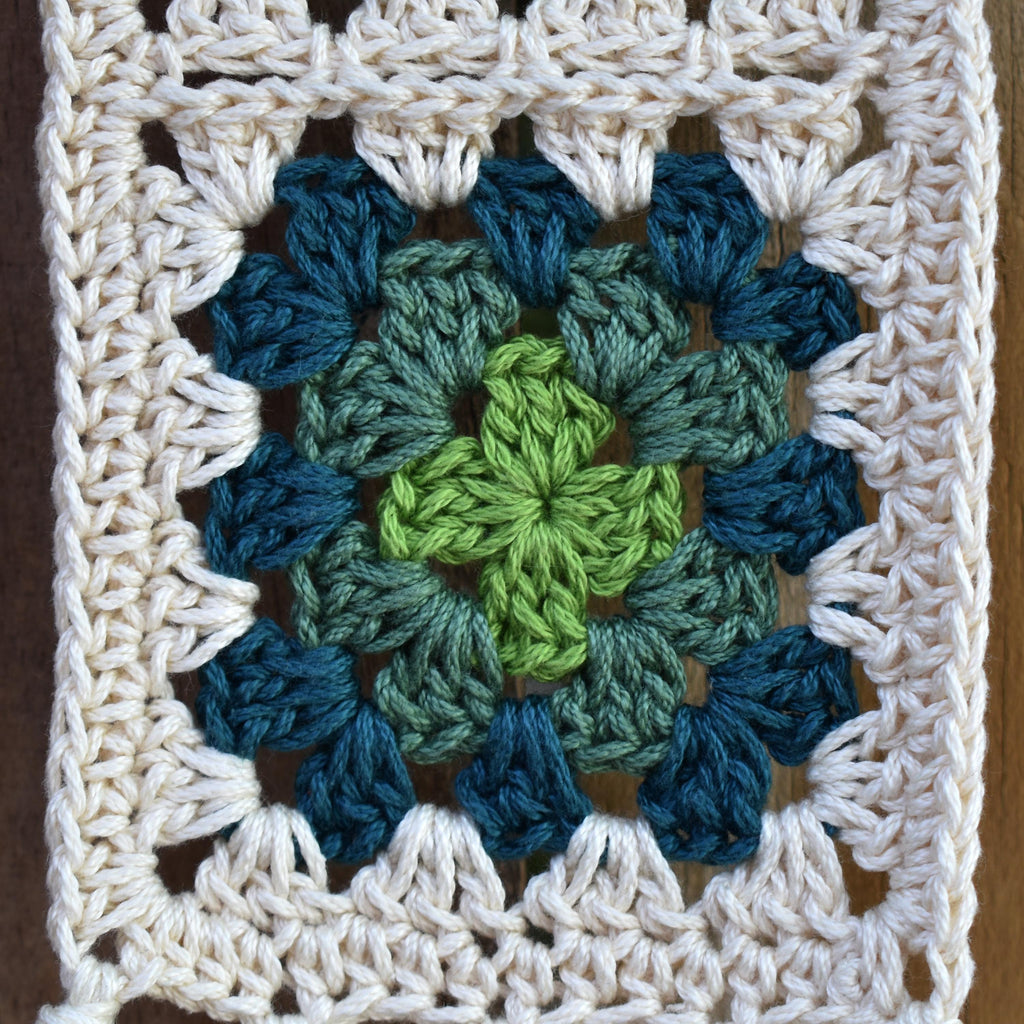 Crocheted granny square with a green and blue pattern on a wooden background.