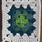 Crocheted granny square with a green and blue pattern on a wooden background.