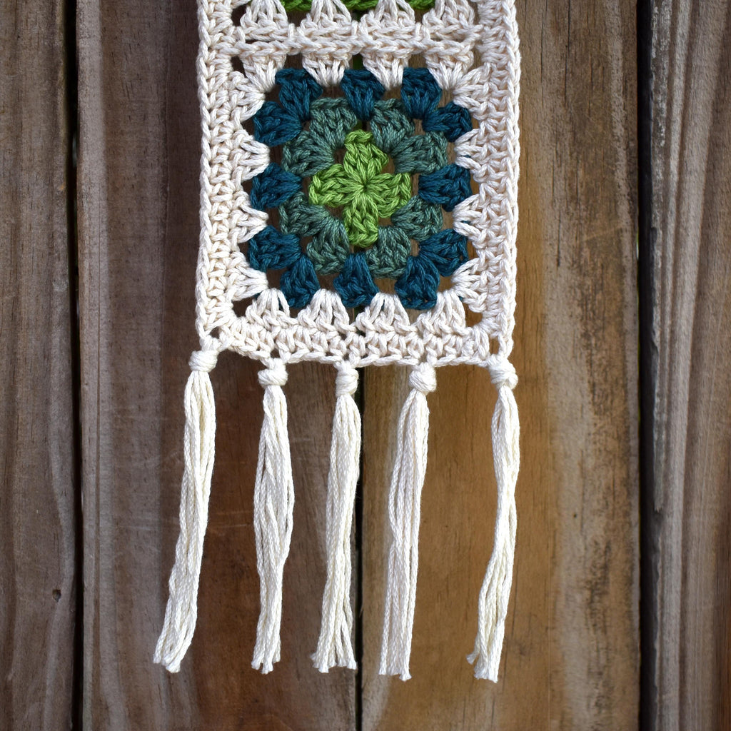 Crocheted wall hanging with a green and blue granny square pattern on a wooden background.