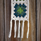 Crocheted wall hanging with a green and blue granny square pattern on a wooden background.