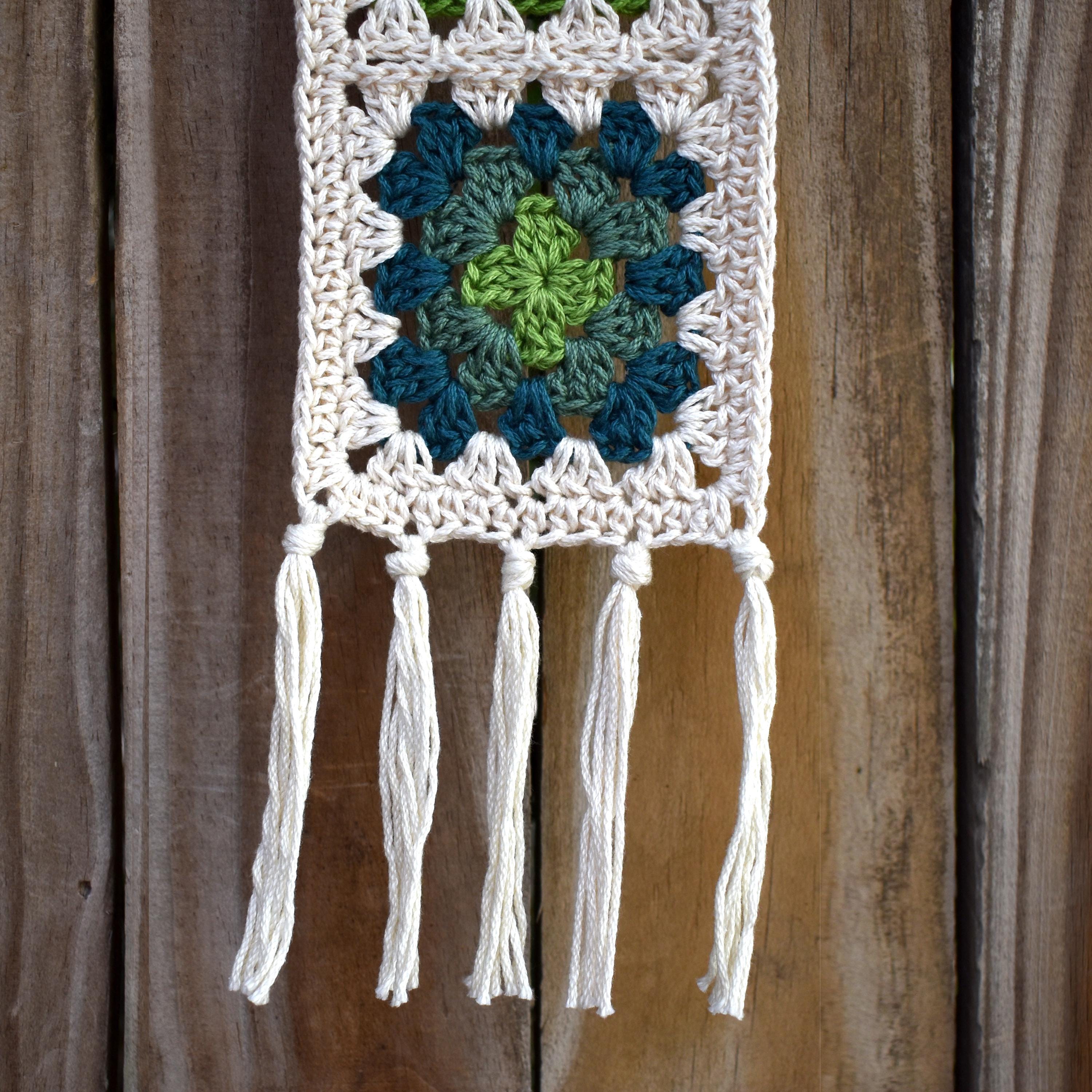 Crocheted wall hanging with a green and blue granny square pattern on a wooden background.
