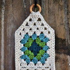 Crocheted wall hanging with a wooden ring on a wooden fence background.