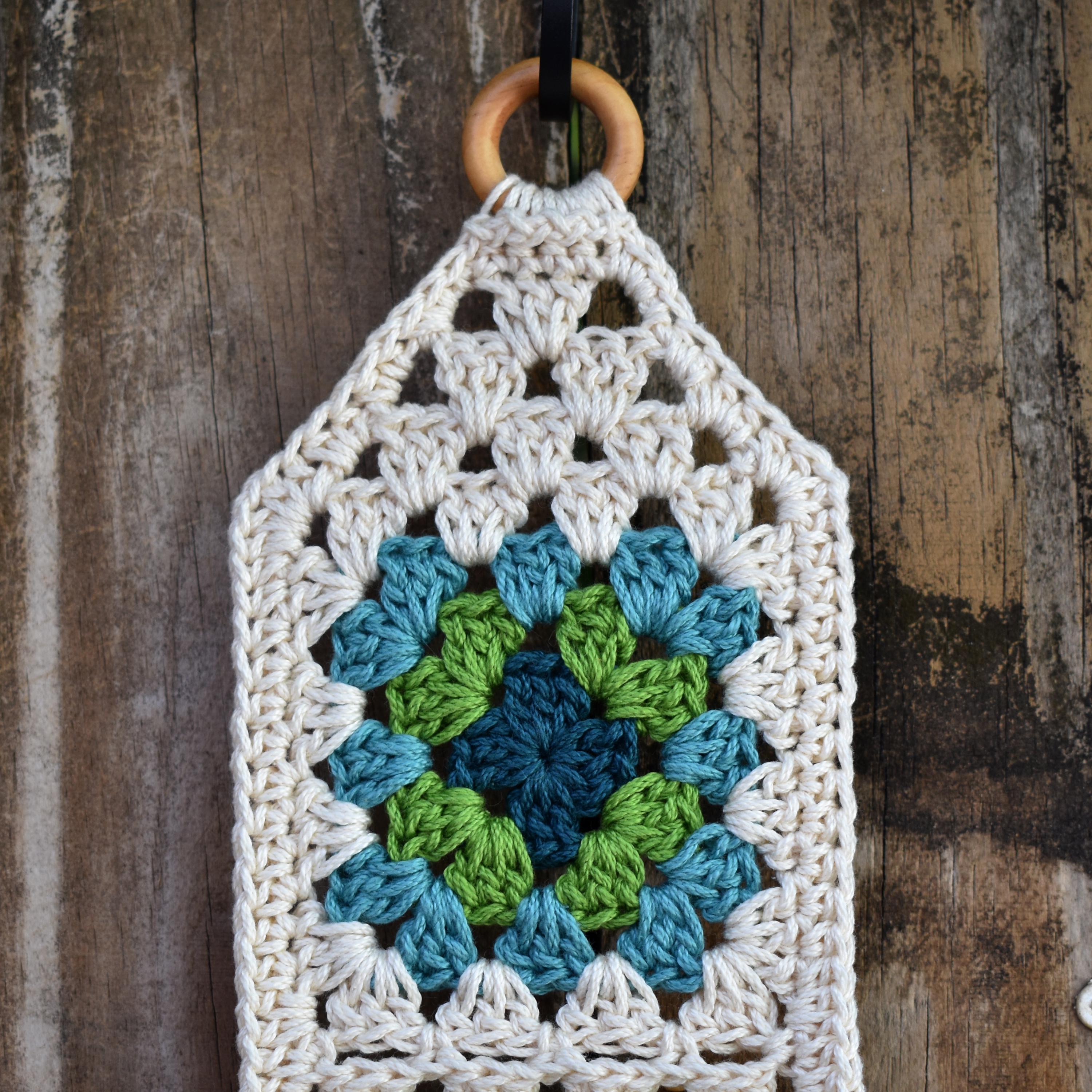 Crocheted wall hanging with a wooden ring on a wooden fence background.
