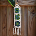 Crocheted wall hanging with geometric pattern and tassels on a wooden background.