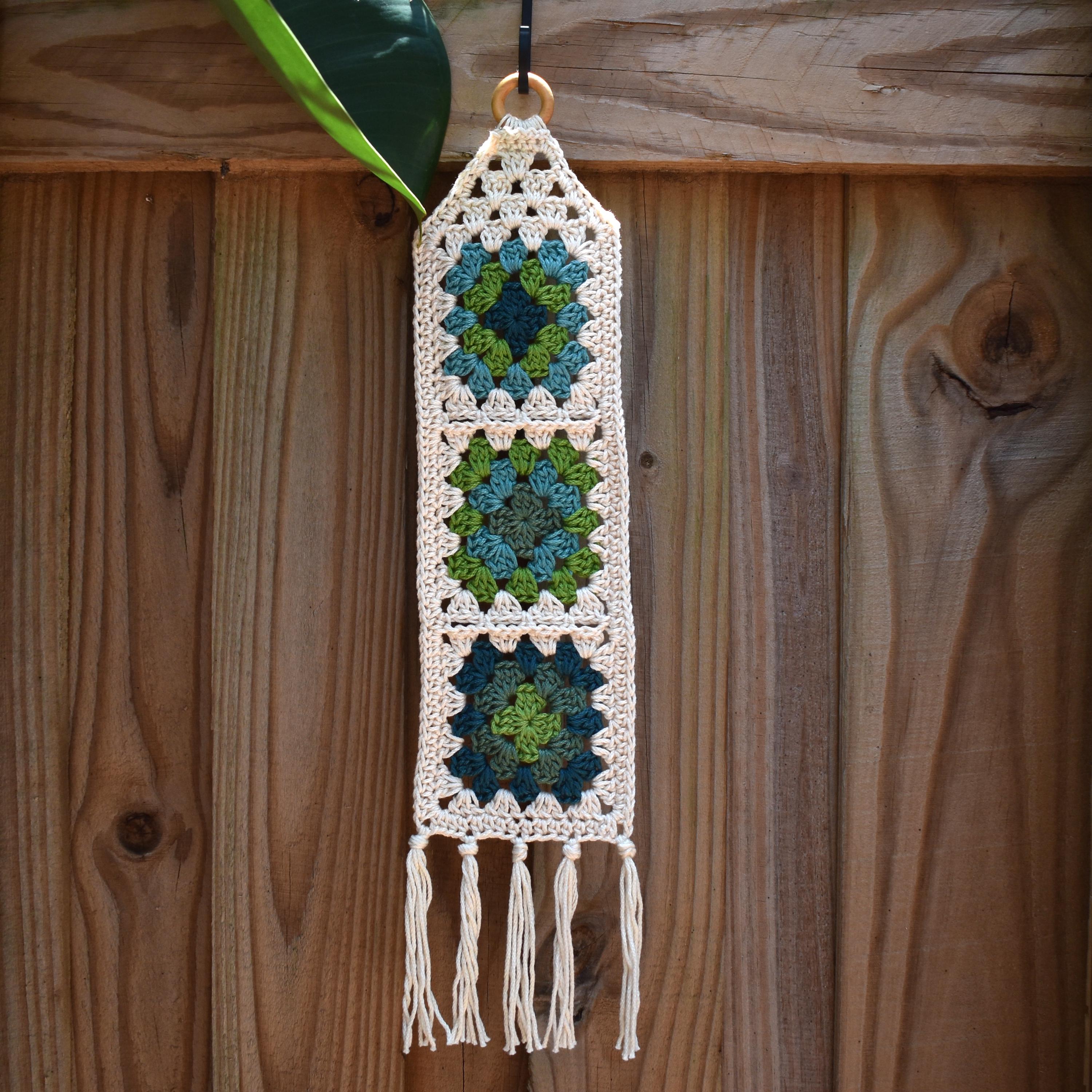 Crocheted wall hanging with geometric pattern and tassels on a wooden background.